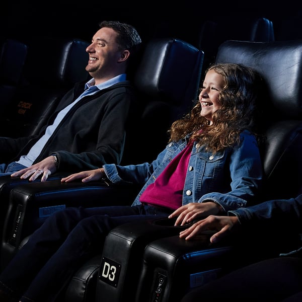 Un père et sa fille assis dans des sièges de cinéma haptiques D-BOX