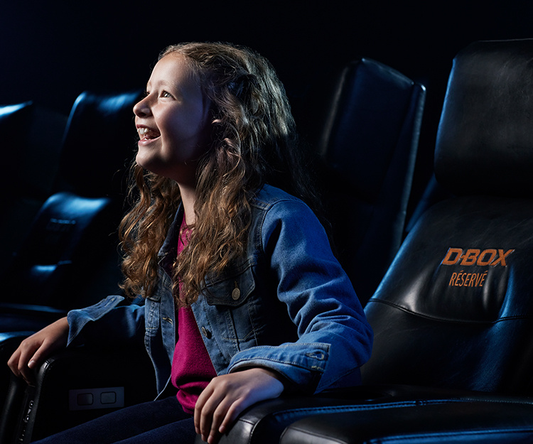 Enfant heureuse regardant un film au cinéma dans un siège D-BOX